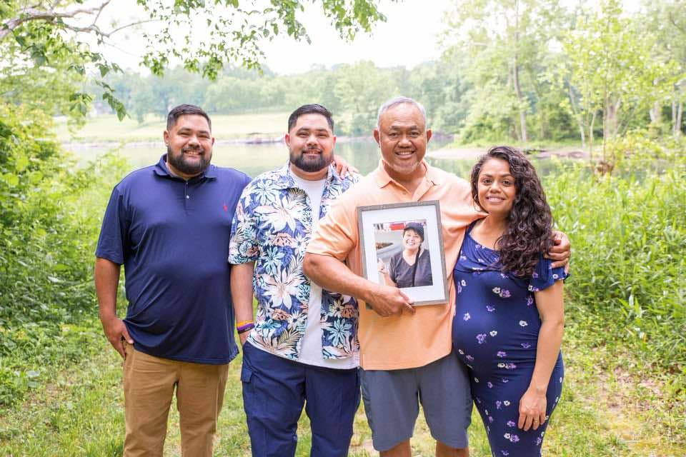 A family holding a framed image of their beloved wife and mother